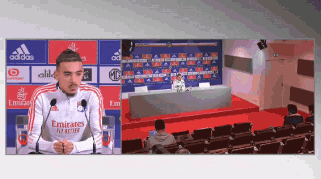 a man wearing a emirates fly better shirt stands in front of microphones
