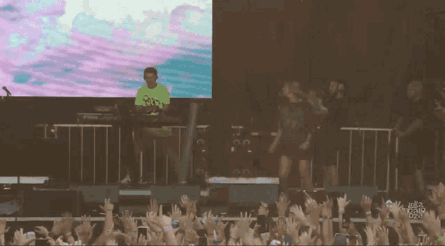 a man in a neon green shirt is playing a keyboard in front of a crowd at a music festival