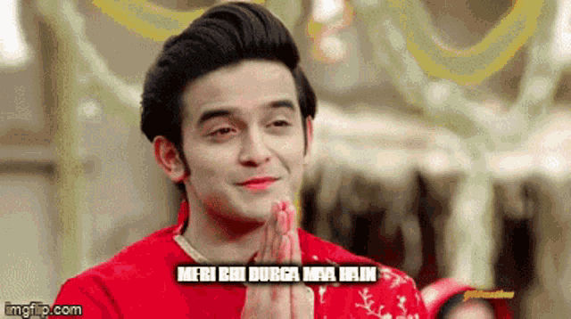 a man in a red shirt is praying with the words meri bi durga maa hain written below him .