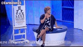 a woman sits on a couch in front of an eye chart with the letters ep on it