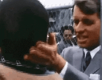 a man in a suit and tie is talking to another man in a crowd .