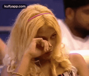 a blonde woman with a pink headband is covering her face with her hand .