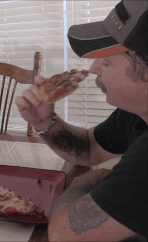 a man is eating a slice of pizza and wearing a hat that says ' a ' on it
