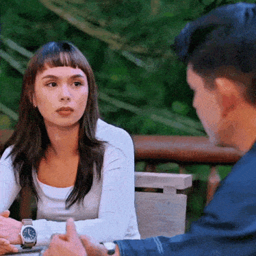 a man and a woman are sitting at a table and the woman has a watch on her wrist that shows the time as 4:20