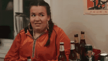 a woman in an orange jacket is sitting at a table with beer bottles and cans