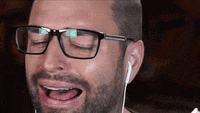 a man with a beard wearing glasses and ear buds is laughing .