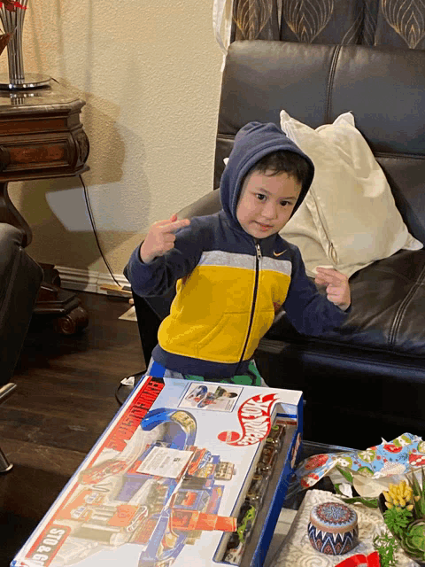 a young boy is standing in front of a box that says hot wheels
