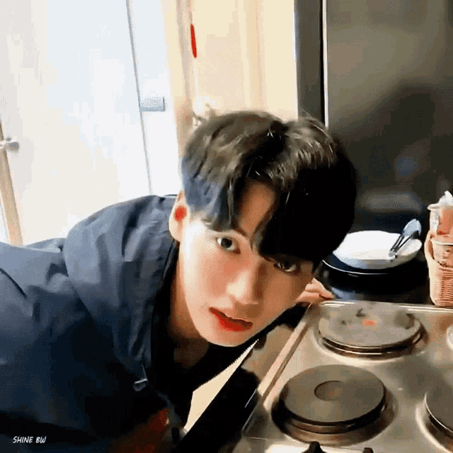a young man is kneeling on a stove and looking at it .