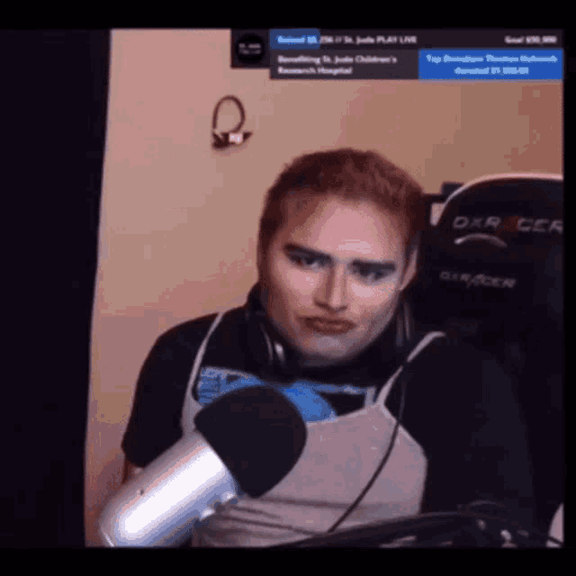 a man sitting in front of a microphone wearing headphones and a dxracer chair