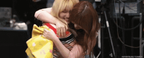 two women are hugging each other in a room while holding a yellow towel .