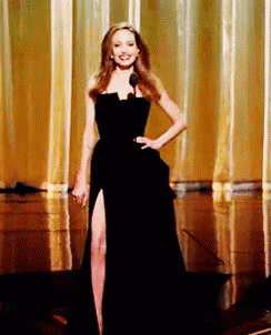 a woman in a black dress is standing on a stage with her hand on her hip
