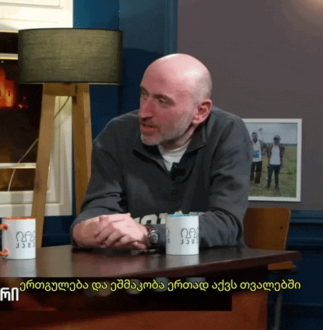 a bald man sits at a table with two coffee cups that say ' 00 ' and ' 330 ' on them
