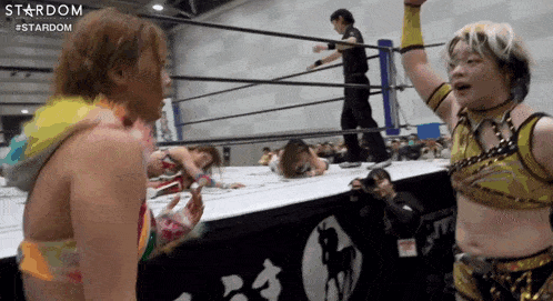 a woman is standing in a wrestling ring with her arms in the air and talking to another woman .