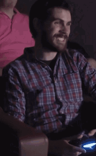a man in a plaid shirt is sitting in a dark room with his eyes closed