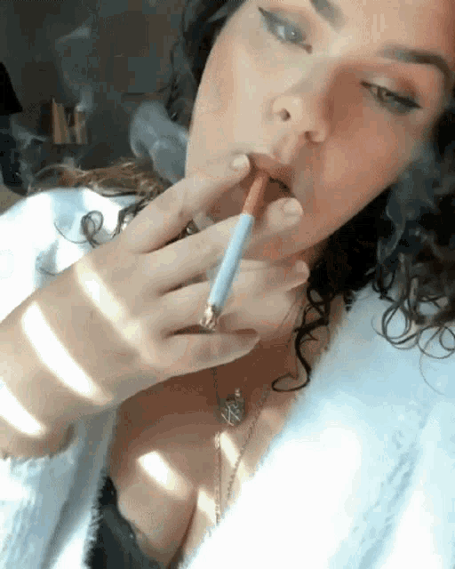 a woman with curly hair is smoking a cigarette while wearing a white robe .
