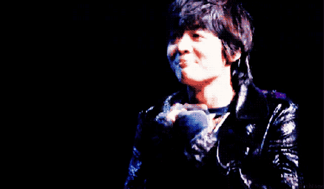 a man in a black jacket is holding a microphone in his hand