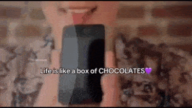 a woman is holding a cell phone with the words life is like a box of chocolates