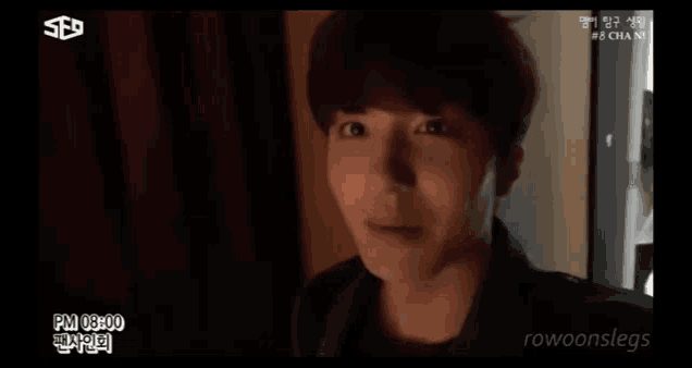 a young man is standing in a dark room with a red curtain behind him .