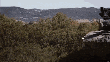 a tank is parked in the middle of a forest with mountains in the background