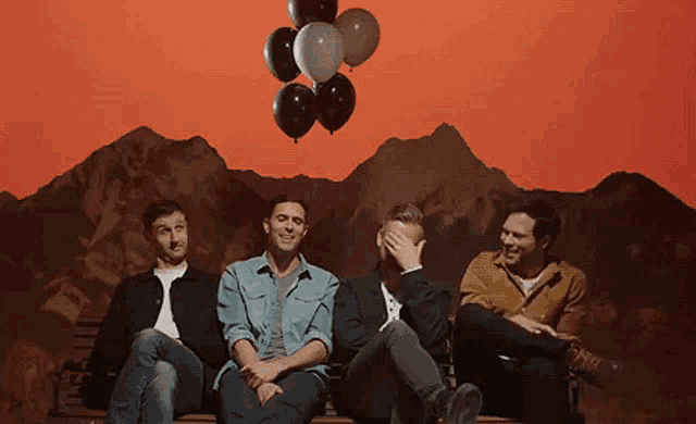 a group of men sit on a bench with balloons floating in the air