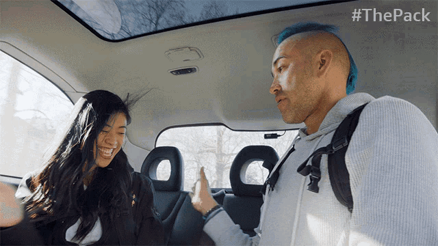 a man with blue hair is giving a woman a high five in a car