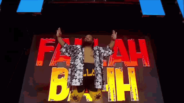 a man in a hawaiian shirt is standing in front of a large screen that says `` fakah buh '' .