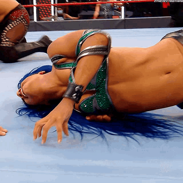 a woman with blue hair is laying on the ground in a wrestling match