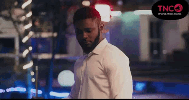 a man in a white shirt is standing in front of a neon sign .