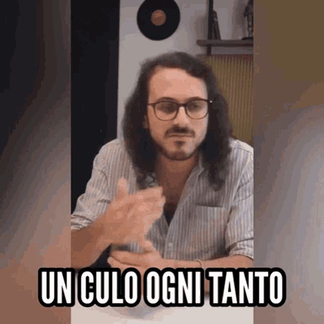 a man with long hair and glasses says " un culo ogni tanto " while sitting at a table