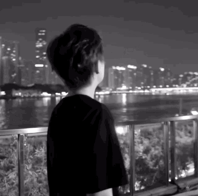 a black and white photo of a person looking out over a body of water .