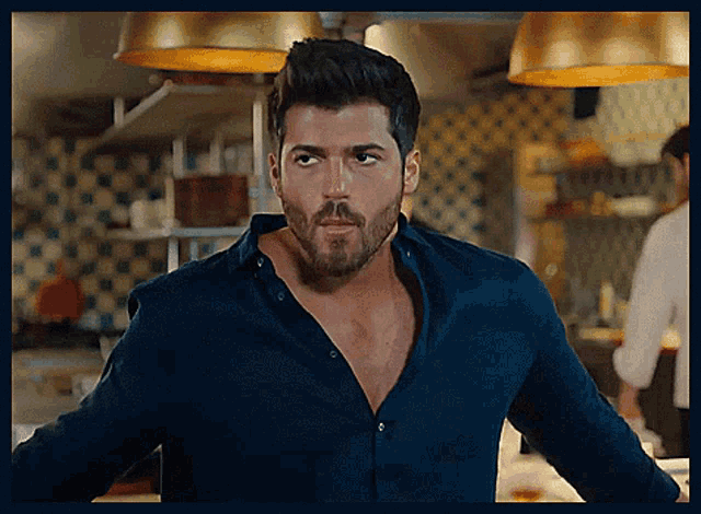a man with a beard is standing in a kitchen wearing a blue shirt