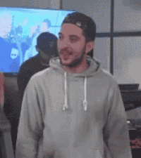 a man wearing a hoodie and a baseball cap is standing in front of a tv .