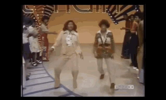 a couple of women are dancing on a stage in front of a crowd of people .