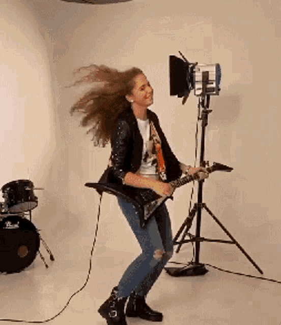 a woman is playing a guitar in front of a pearl drum set