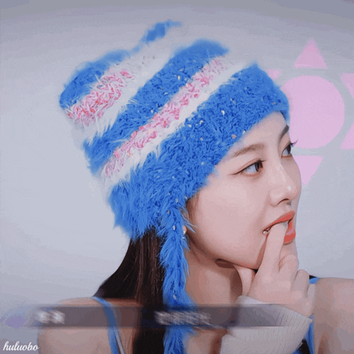 a woman wearing a blue and white striped hat is smiling and holding her finger to her lips