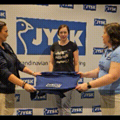 three women are holding a blue t-shirt in front of a jysk sign