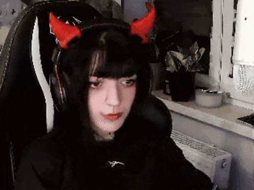 a girl wearing headphones and red horns is sitting in a chair .