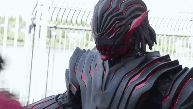a person in a black and red costume is standing in front of a white fence