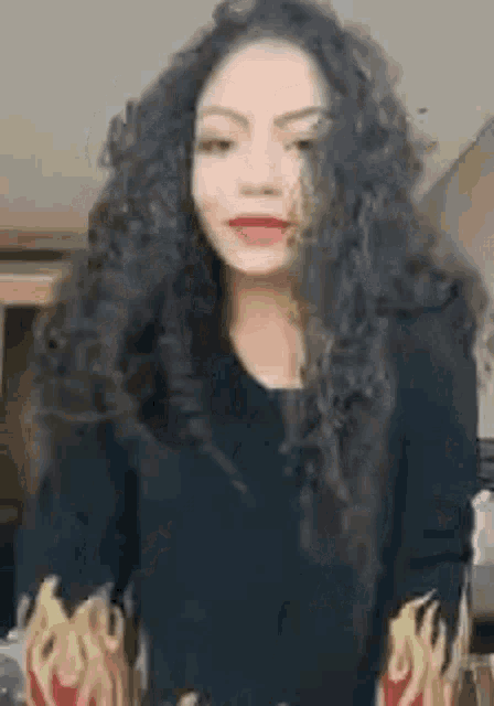 a woman with long curly hair wearing a black sweater with flames on the sleeves .