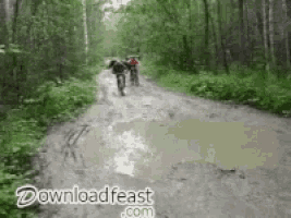 a couple of people riding bikes down a muddy road .