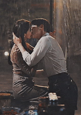 a man and a woman are kissing in the rain while sitting on a bench .
