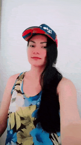 a woman wearing a baseball cap and a floral tank top is taking a selfie .