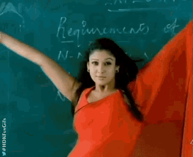 a woman in a red shirt is standing in front of a blackboard with her arms in the air .
