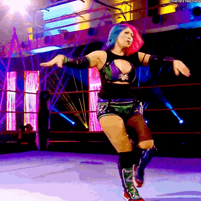 a woman with pink and blue hair is dancing in a wrestling ring
