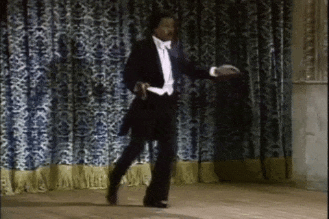 a man in a tuxedo is dancing on a stage in front of a blue curtain .