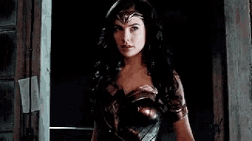wonder woman is standing in front of a door in a dark room .