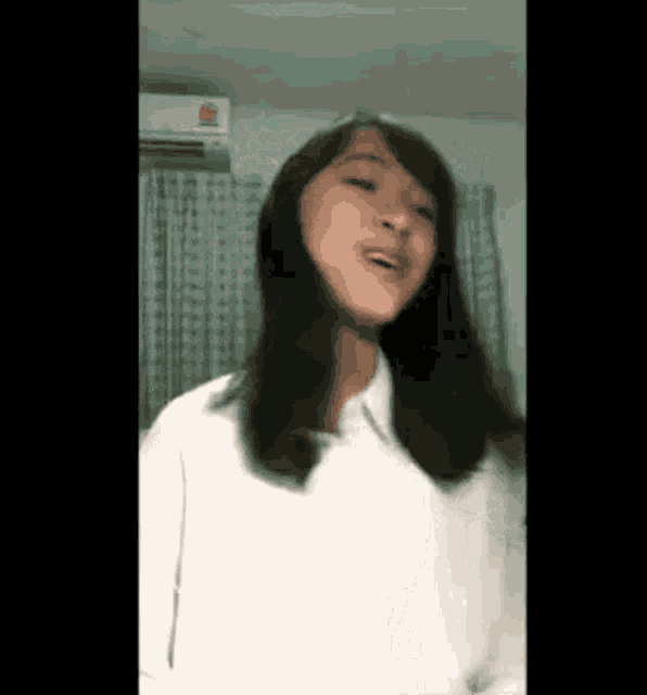 a girl in a white shirt is dancing in front of a window
