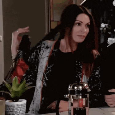 a woman sitting at a table with a french press in her hand