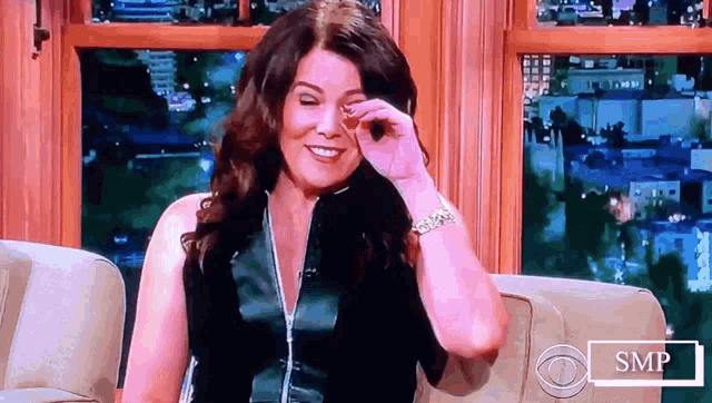 a woman wipes her eye while sitting on a couch in front of a cbs logo