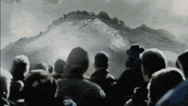 a large group of people are standing in front of a mountain looking at it .